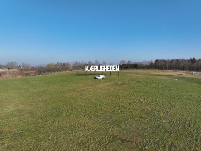 Bil på en mark med et stort skilt, hvor der står Kærligheden