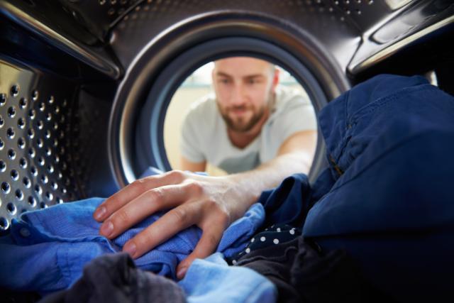 En mand putter tøj i sin vaskemaskine.