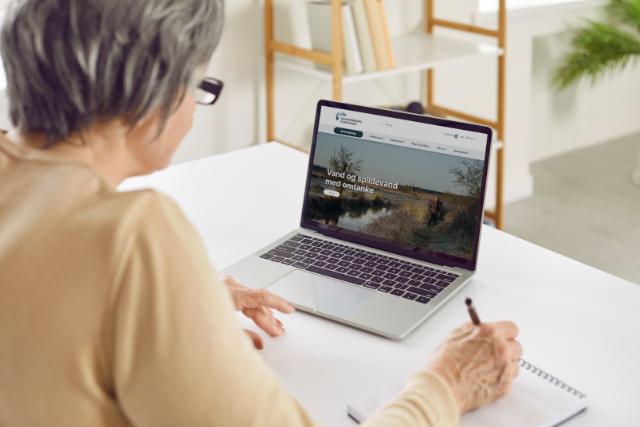 En dame sidder ved en bærbar computer, med forsyningens hjemmeside på skærmen