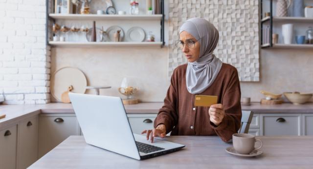 En dame sidder ved sin bærbare computer med et betalingskort